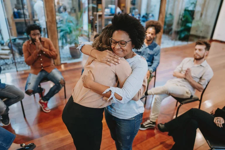Young support group women hugging with other people supporting sitting in chairs.