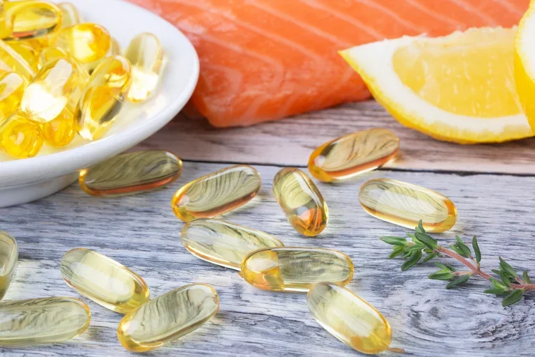 a handfull of fish oil vitamin supplement, a slice of lemon and salmon on a wooden table