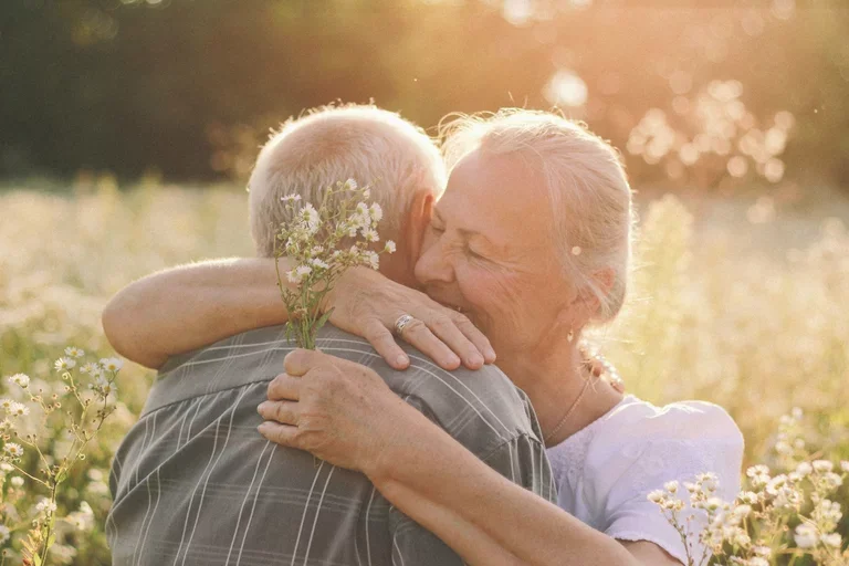 caucasian woman hugging and comforting her spouse in the middle of a field of flowers.