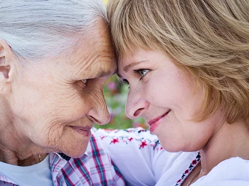 Elderly mother and adult daughter looking into each other's eyes, smiling with a sense of support.