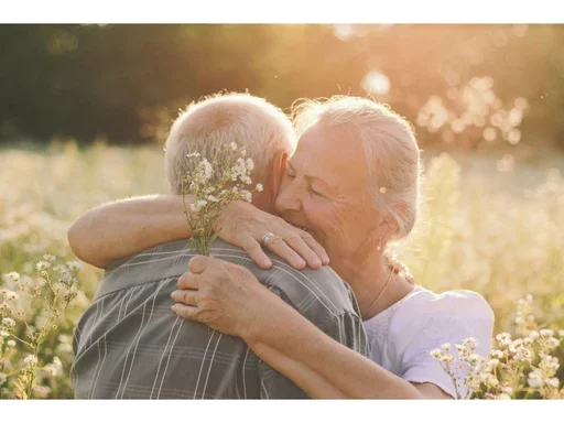 caucasian woman hugging and comforting her spouse in the middle of a field of flowers.